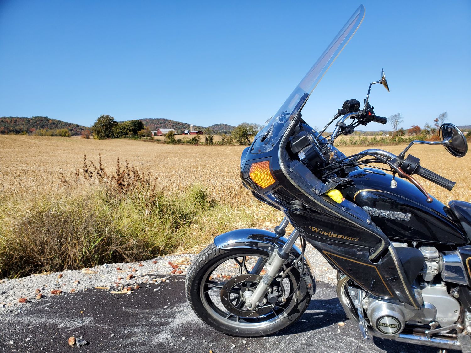A motorcycle pulled over on a back road beside a farm field